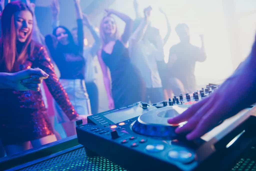 DJ playing stereo loud sound rhythm set for attractive, stylish, cheerful positive people crowd to hang out enjoying evening having fun time festive concert at a fashionable modern nightclub
