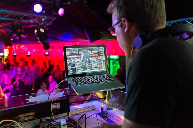 A male disc jockey (DJ) that is playing two tracks at the same time on his laptop