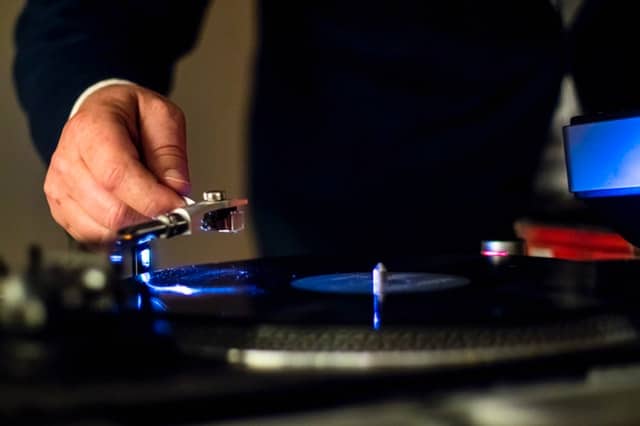 A male holding the cartridge of a vinyl player above a playable record