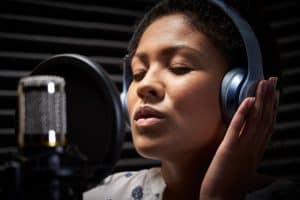 Female vocalist wearing headphones singing into a microphone in a recording studio
